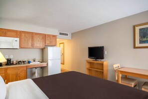 A hotel room with a bed, a desk, a television, a microwave, a refrigerator, and wooden cabinets.