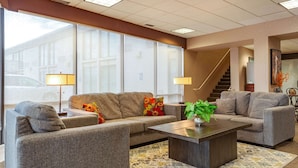 A modern hotel lobby with a grey sofa set, a coffee table, and a staircase. - Suburban Studios I-80 Grand Island (Grand Island)