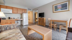 A compact living space with a kitchenette, a dining area, a TV, and a painting on the wall. - Suburban Studios I-80 Grand Island (Grand Island)