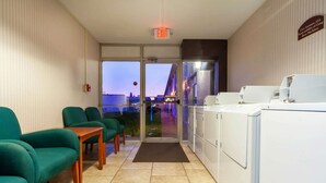 A hotel lobby with green chairs, a reception desk, and a view of the outside at dusk.