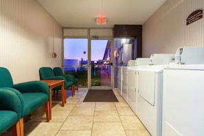 A hotel lobby with green chairs, a reception desk, and a view of the outside at dusk.