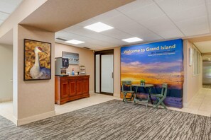 A reception area with a welcome banner, a reception desk, a framed artwork, and a seating area with a table and chairs. - Suburban Studios I-80 Grand Island (Grand Island)