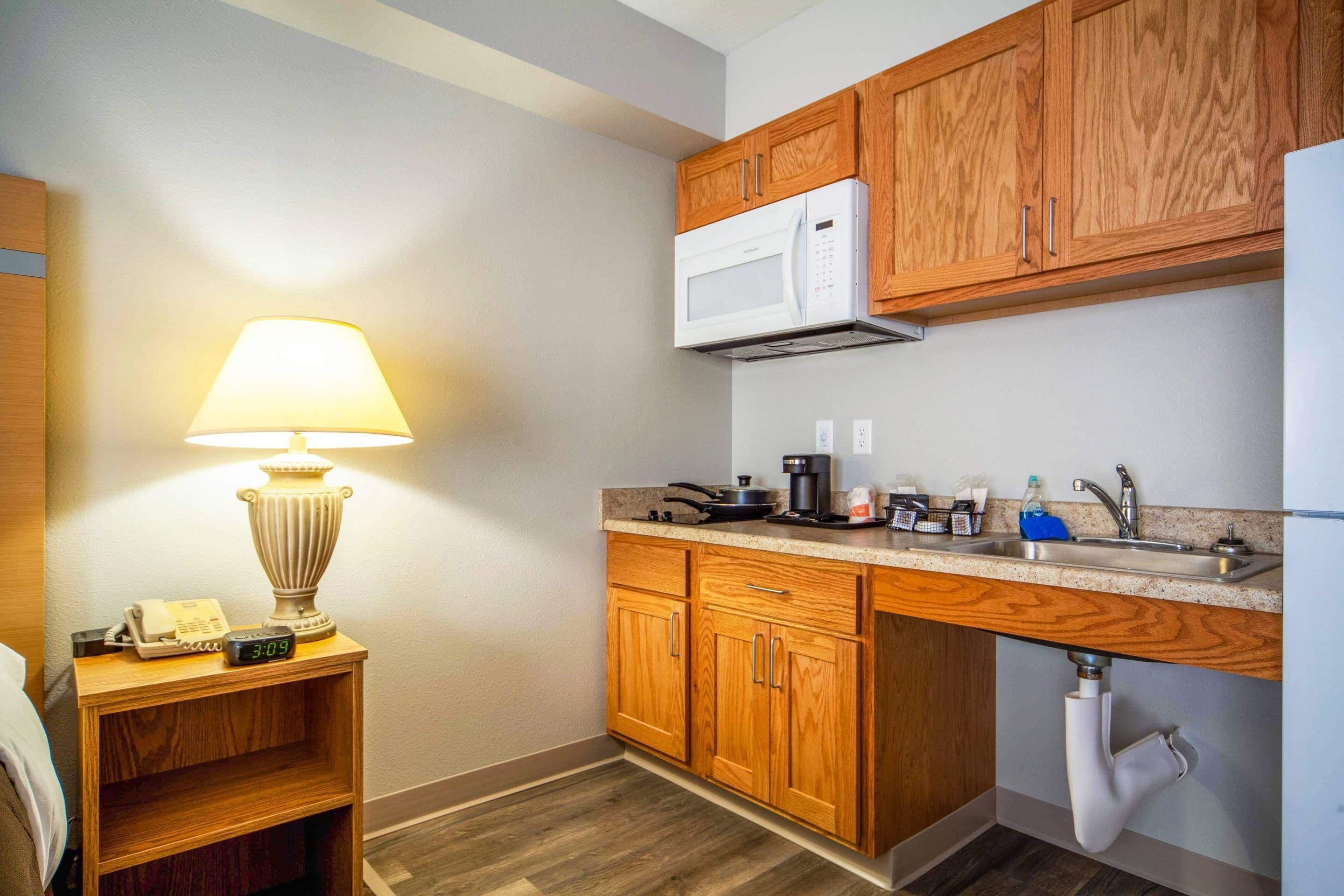 Cocina compacta con armarios de madera, microondas, lavabo y encimera con diversos objetos.
