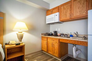 A compact kitchen with wooden cabinets, a microwave, a sink, and a countertop with various items.