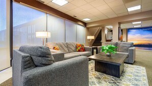 A modern hotel lobby with grey sofas, a wooden coffee table, and a large window. - Suburban Studios I-80 Grand Island (Grand Island)