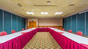Un salón de conferencias con una mesa larga, sillas y una alfombra estampada.
