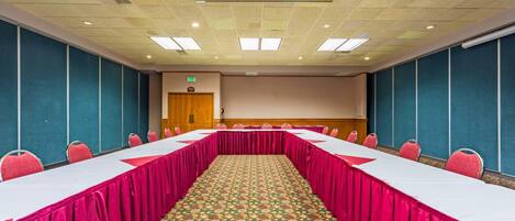 Un salón de conferencias con una mesa larga, sillas y una alfombra estampada.