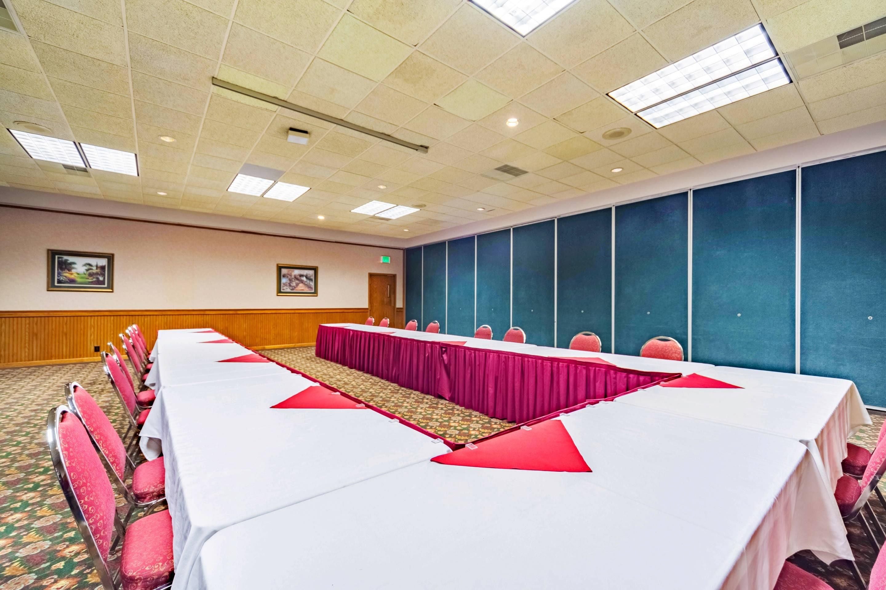 Un salón de conferencias con una larga mesa, sillas rojas y un tabique azul.