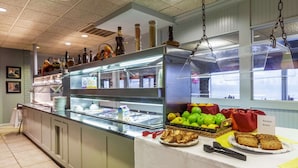 A buffet area with a glass display case, a variety of fruits, and a sign indicating 'Banana Bread'. - Suburban Studios I-80 Grand Island (Grand Island)