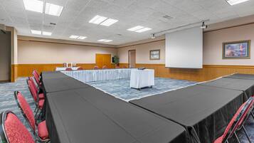 A conference room with a long table, red chairs, a projector screen, and a painting on the wall.