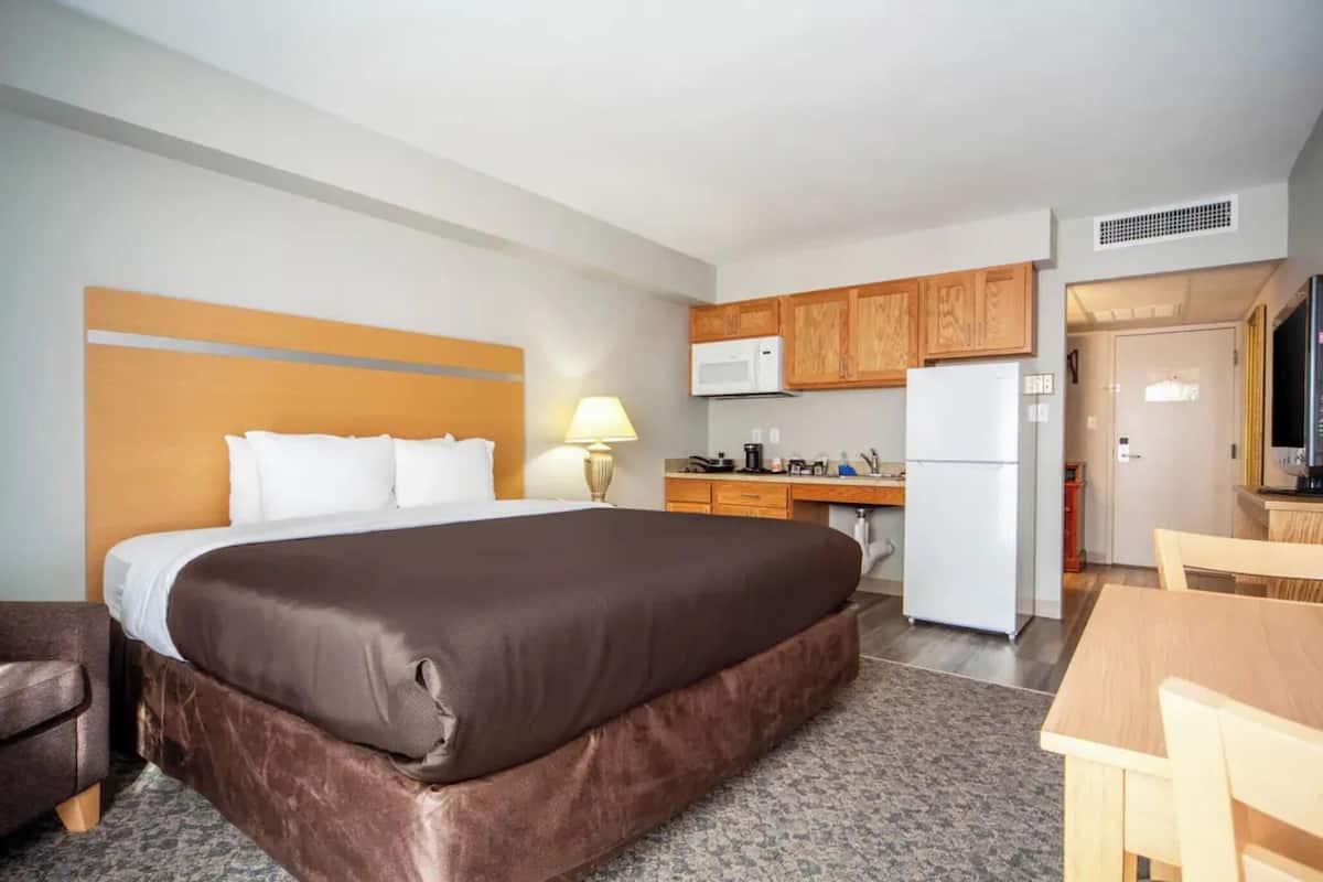 A hotel room with a bed, a desk, a microwave, a refrigerator, and a kitchenette.