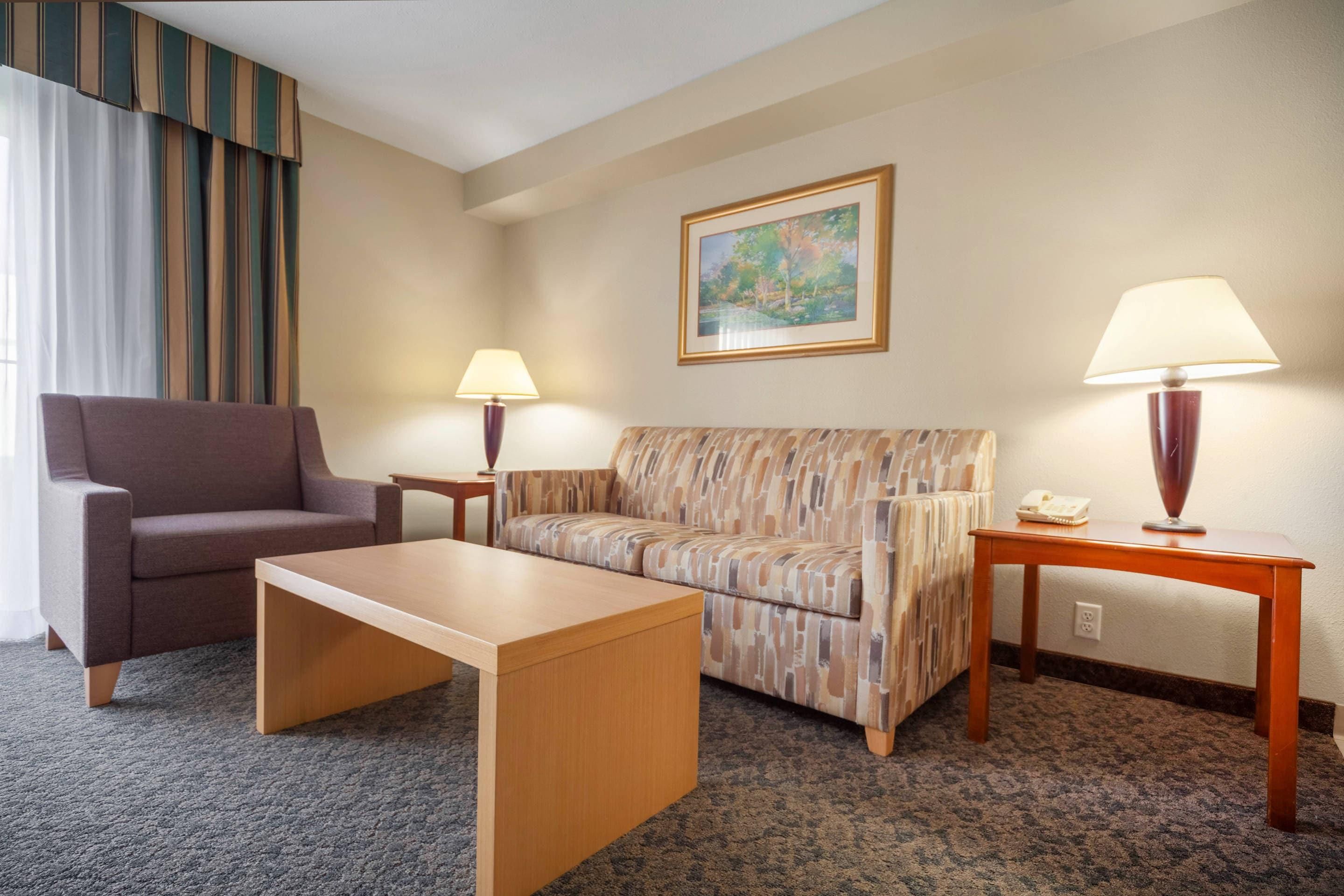 Una habitación de hotel con sofá, una silla, una mesita y una lámpara.