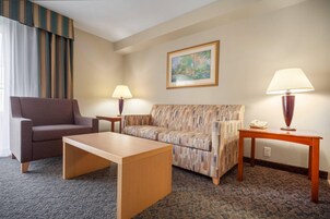 Una habitación de hotel con sofá, una silla, una mesita y una lámpara.