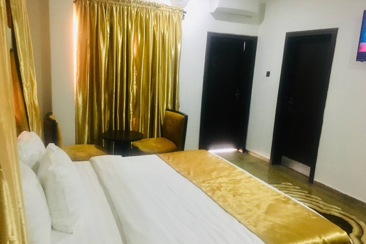 A hotel room with a large bed, two chairs, a small table, and a curtain.