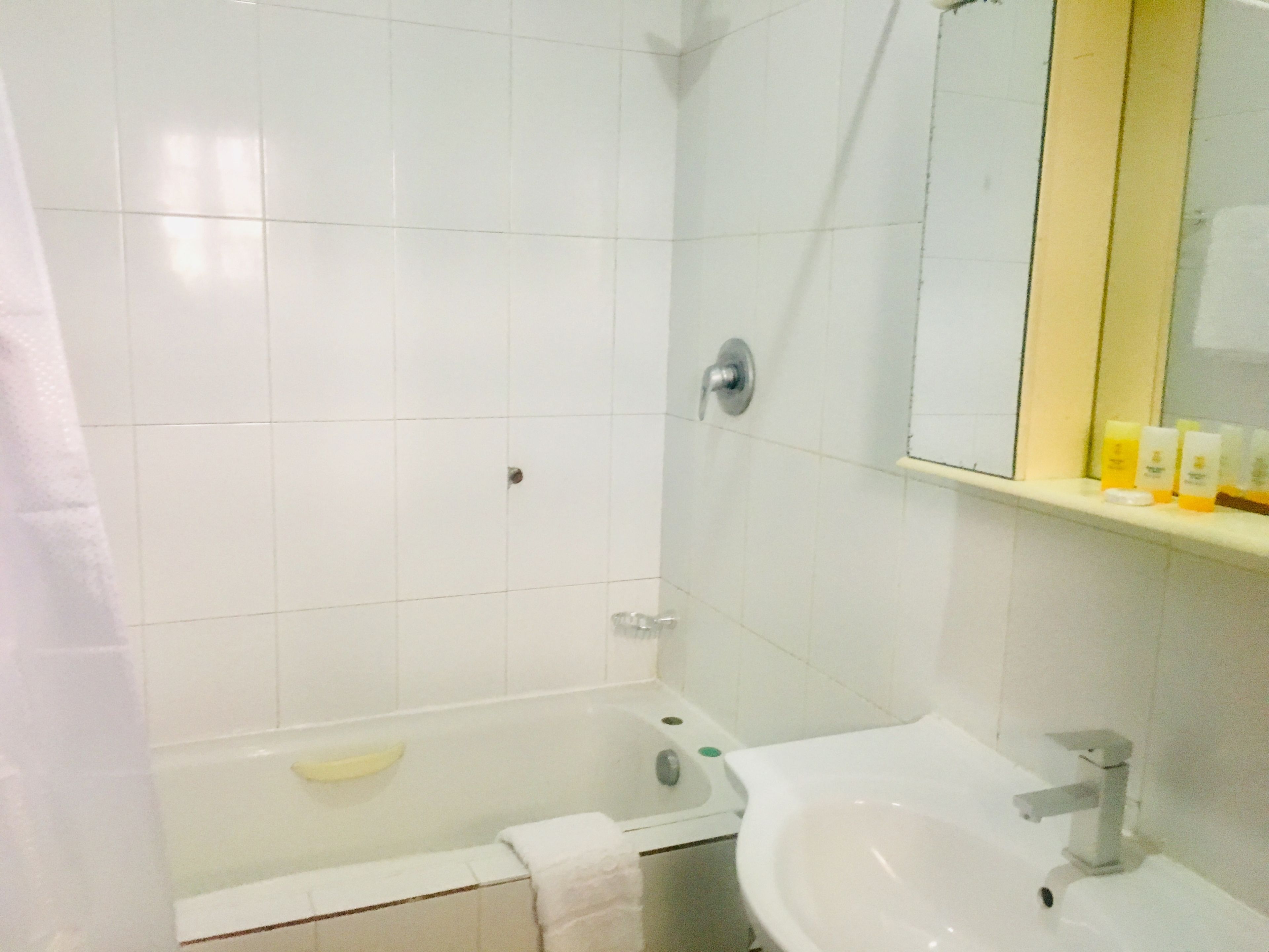 A bathroom with white tiles, a bathtub, a sink, and a mirror.