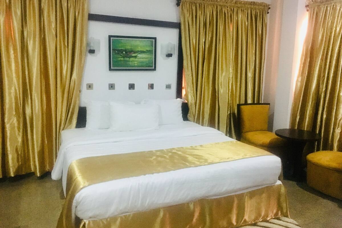 A hotel room with a bed, a chair, a small table, and a painting on the wall.