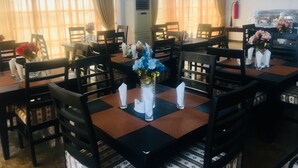 A dining area with tables set for four, each with a vase of flowers and a candle. There are multiple chairs around the tables, and a television is mounted on the wall. - Blue Moon Beach Hotel & Resort (Lagos)