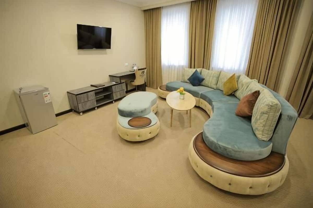 A living room with a sectional sofa, ottoman, small round table, TV, and a minibar.