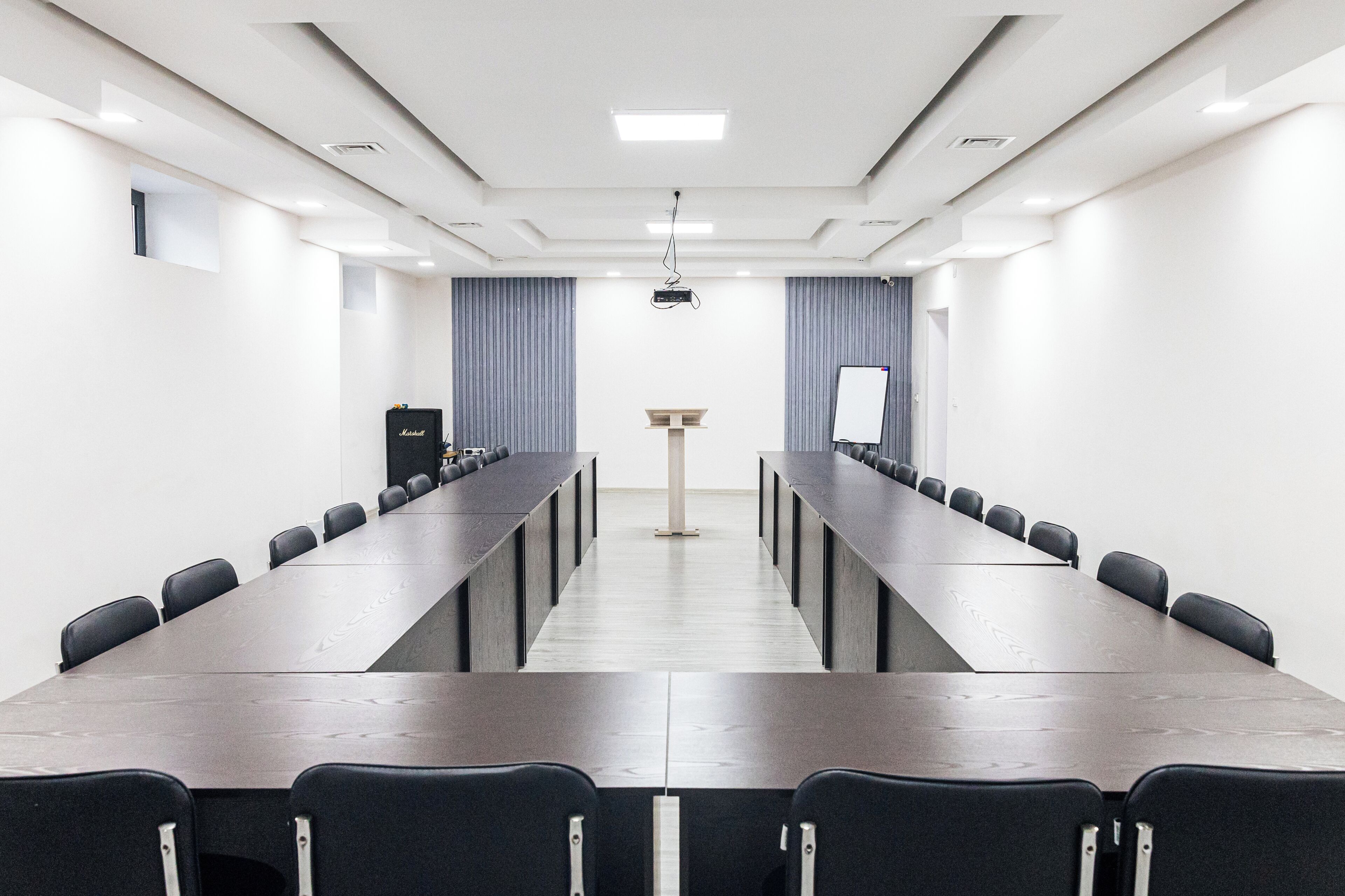 Un salón de conferencias con una larga mesa, filas de sillas, un atril y cortinas.
