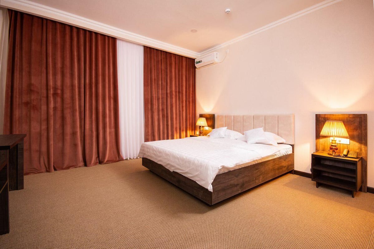 A hotel room with a large bed, a nightstand with a lamp, and a wall-mounted air conditioning unit.