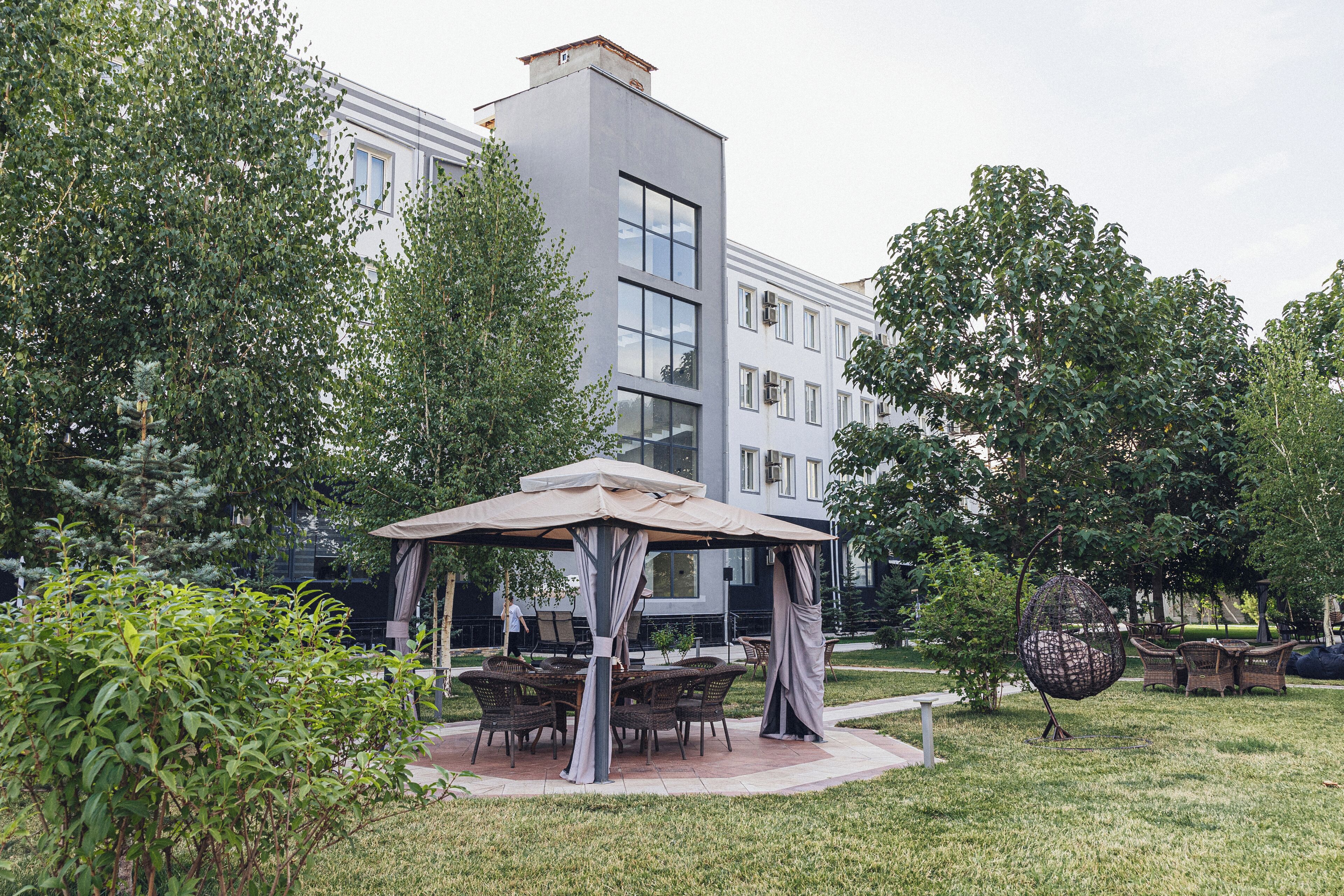 A modern building with a patio area featuring a gazebo, wicker furniture, and a hanging chair.