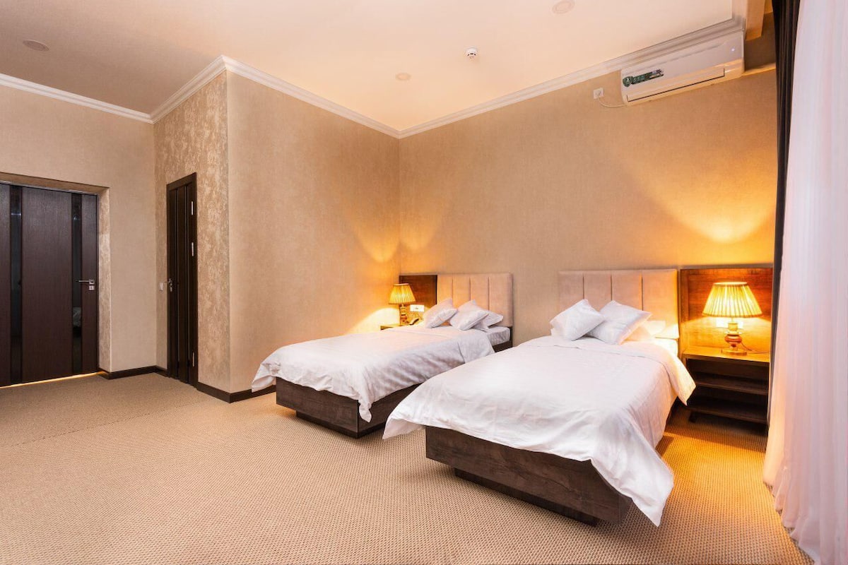 A hotel room with two beds, a door, and a wall-mounted air conditioning unit.