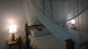 Een slaapkamer met een hemelbed, nachtlampjes en een nachtkastje met een bloemstuk.
