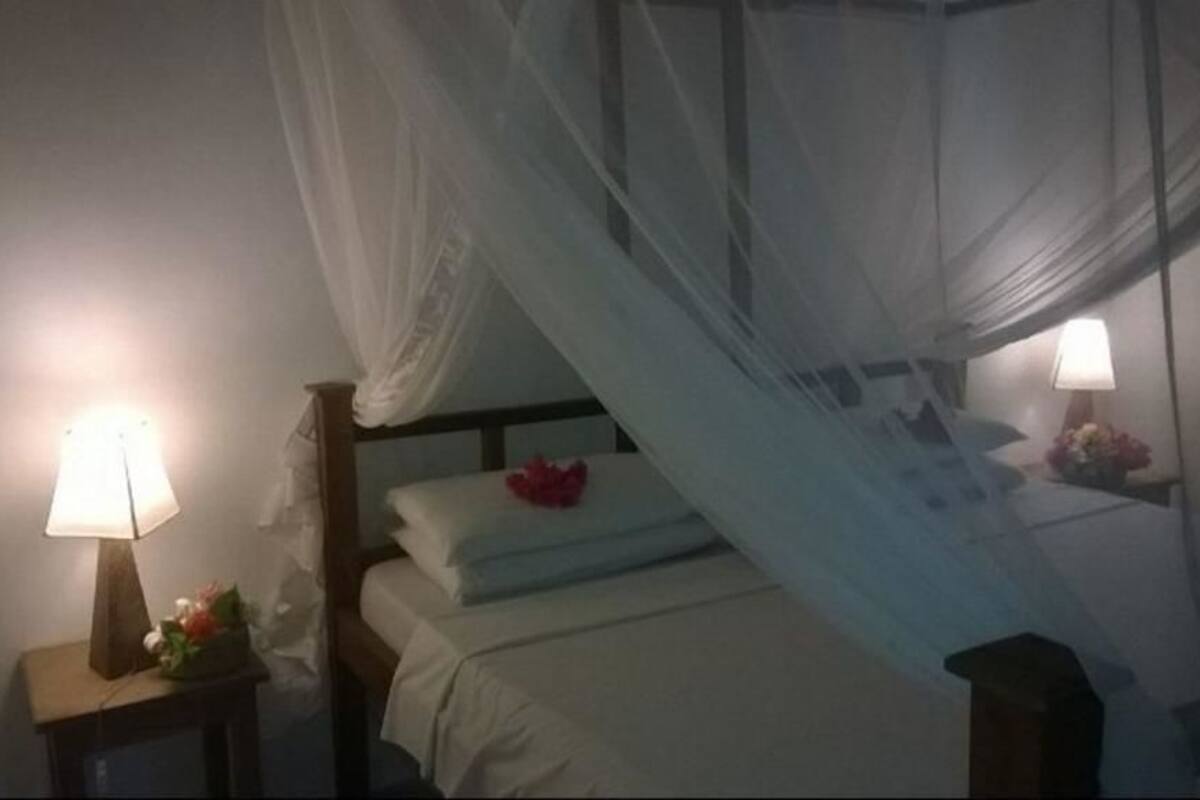 A bedroom with a canopy bed, bedside lamps, and a nightstand with a flower arrangement.