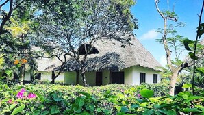 Een rieten huis omgeven door weelderige begroeiing en bloeiende planten.