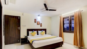 A hotel room with a bed, a ceiling fan, a nightstand, a window with curtains, and a door. - Itsy Hotels Royal Monarch (Gorakhpur)