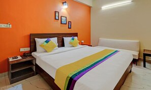 Una habitación de hotel con pared naranja, estructura de cama de madera, ropa de cama blanca y una manta de colores del arcoíris.