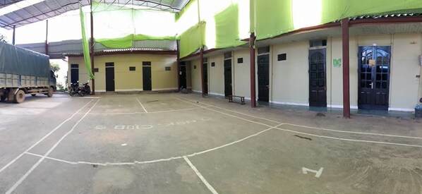 An indoor sports court with a basketball hoop, a covered area with green netting, and a truck parked outside.