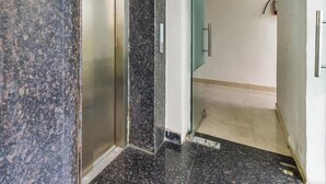 Un ascensor con pared de mármol y señal de salida verde.