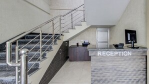 Un área de recepción con mostrador de mármol, una escalera con barandilla de metal y una puerta al fondo.