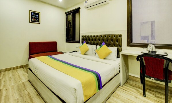 Una habitación de hotel con cama, escritorio, silla, aire acondicionado y ventana.