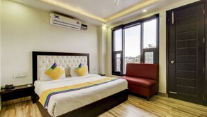 Una habitación de hotel con cama, una silla roja, unidad de aire acondicionado, ventana y puerta.