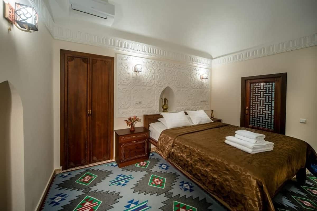 Une chambre à coucher avec un lit, une armoire en bois, une table de chevet et un tapis à motifs.