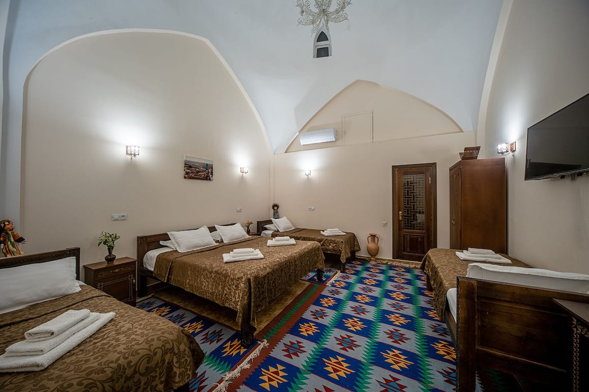 Une chambre avec deux lits, un téléviseur, une armoire en bois et un tapis à motifs.