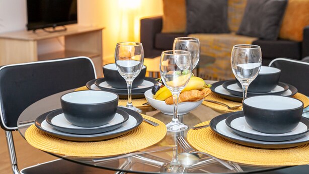 A dining table set with black bowls, plates, and wine glasses, with a bowl of fruit and croissants in the center. - Stunning Manchester Apartment (Salford)