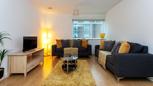 A modern living room with a sofa set, a TV, and a floor lamp. - Stunning Manchester Apartment (Salford)