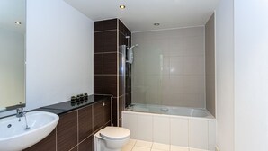 A modern bathroom with a white sink, dark brown tiles, a toilet, and a glass-enclosed shower. - Stunning Manchester Apartment (Salford)