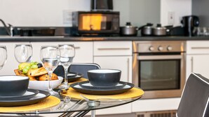 A modern kitchen with a dining table set for two, featuring a bowl of fruit, wine glasses, and plates. - Stunning Manchester Apartment (Salford)