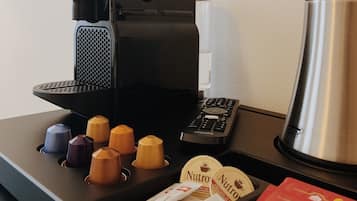 Uma cafeteira, um controle remoto e uma bandeja com cápsulas de café e um sachê de creme para café.