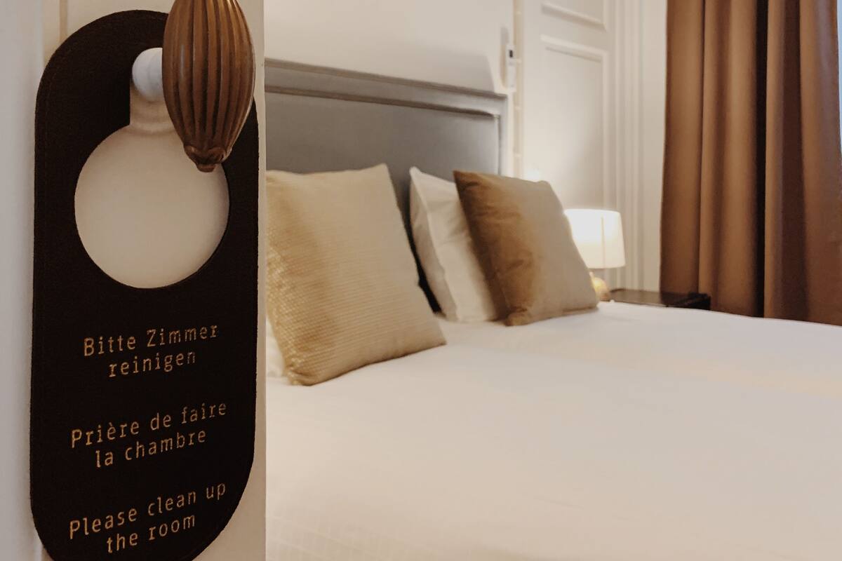 Une chambre d’hôtel équipée d’un lit, d’oreillers, d’un climatiseur fixé au mur et d’une pancarte demandant le nettoyage de la chambre.