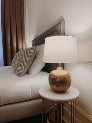 Un lit bien fait, avec un oreiller à motifs, une lampe de chevet posée sur une petite table ronde et une tête de lit.