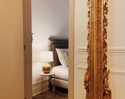 A hotel room with a bed, a bedside table with a lamp, and a decorative golden mirror.