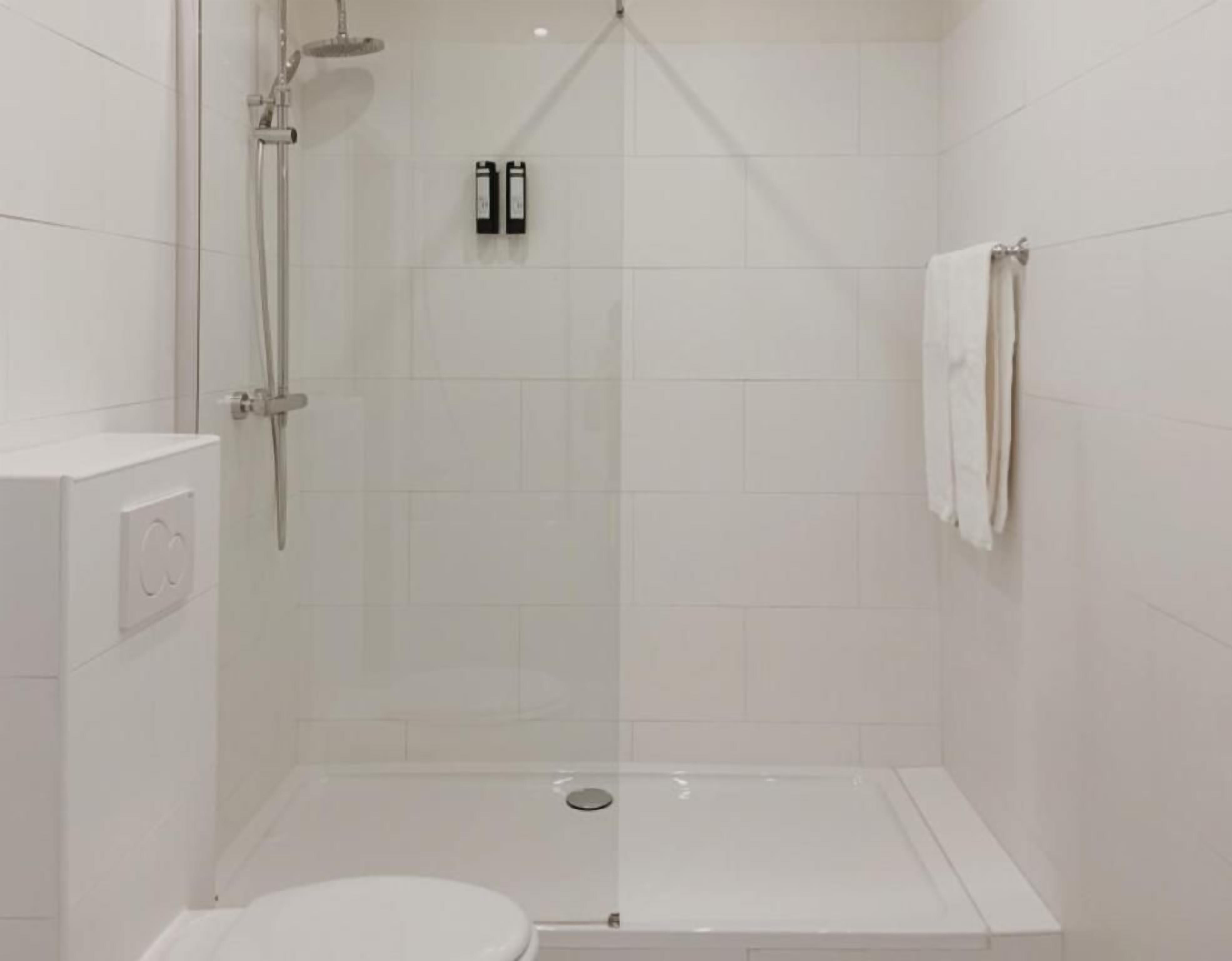 Un box de ducha pequeño y cerrado con puerta de vidrio, un inodoro blanco y una toalla colgada en la pared.