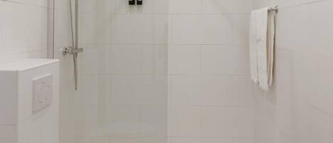 Un box de ducha pequeño y cerrado con puerta de vidrio, un inodoro blanco y una toalla colgada en la pared.