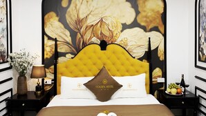Ein Hotelzimmer mit einem großen Bett, einem Blumenmuster an der Kopfteil, einem Nachttisch mit Lampe und einer Wand mit gerahmten Kunstwerken.
