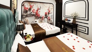 Ein Hotelzimmer mit einem großen Bett, einem Nachttisch mit Lampe, einem kleinen Tisch mit Früchten und einer Flasche sowie einer Wand mit einem dekorativen Gemälde.